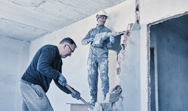 Zwei Personen mitten im Abriss einer Zwischenwand einer Wohnung